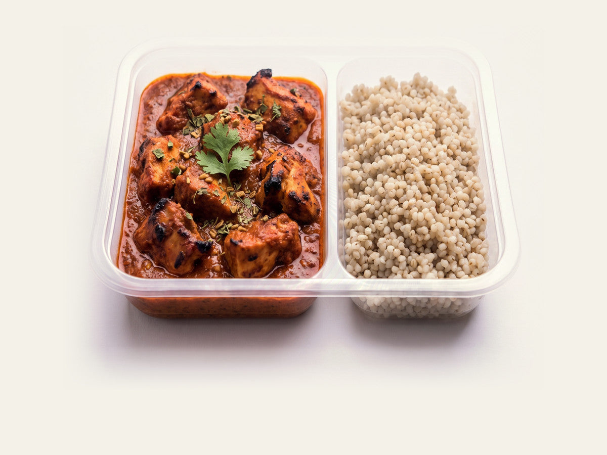 A retort tray of Fuel Chicken Tikka Masala beside its millet compartment, on a plain cream studio background.